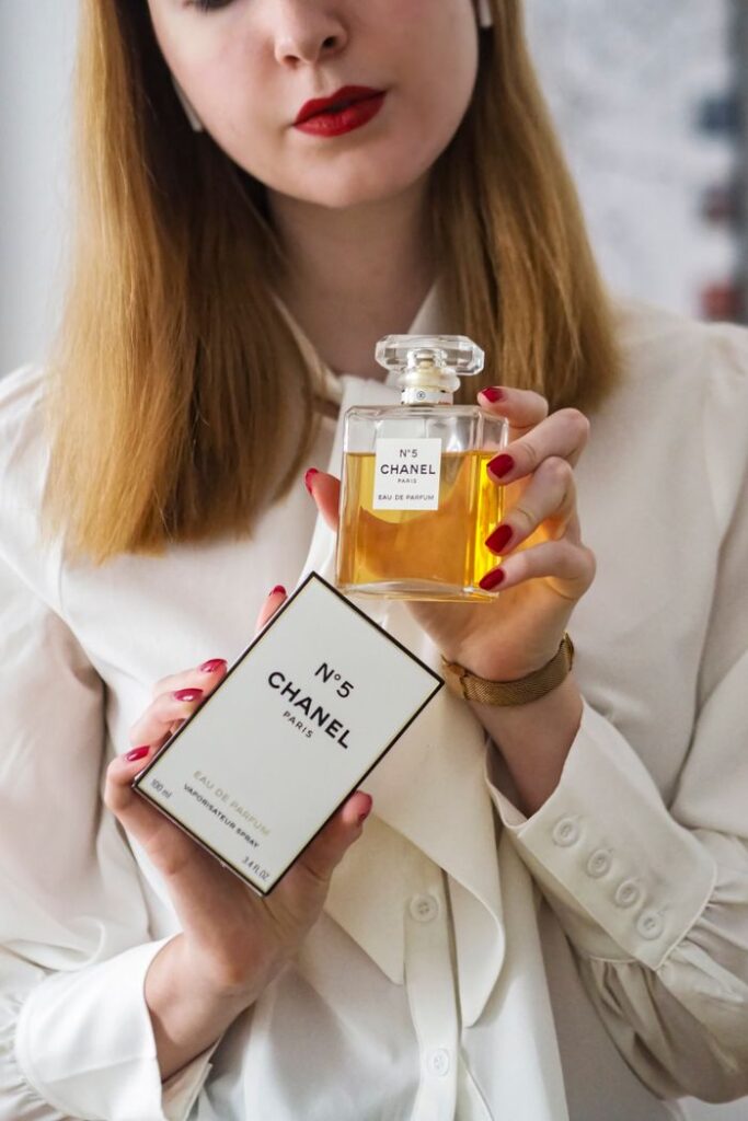 Woman displaying Chanel No.5 perfume against a neutral background with elegant attire.
