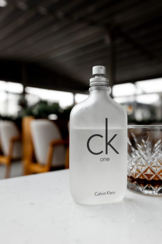 Sophisticated CK One perfume bottle with glass, set on outdoor cafe table.